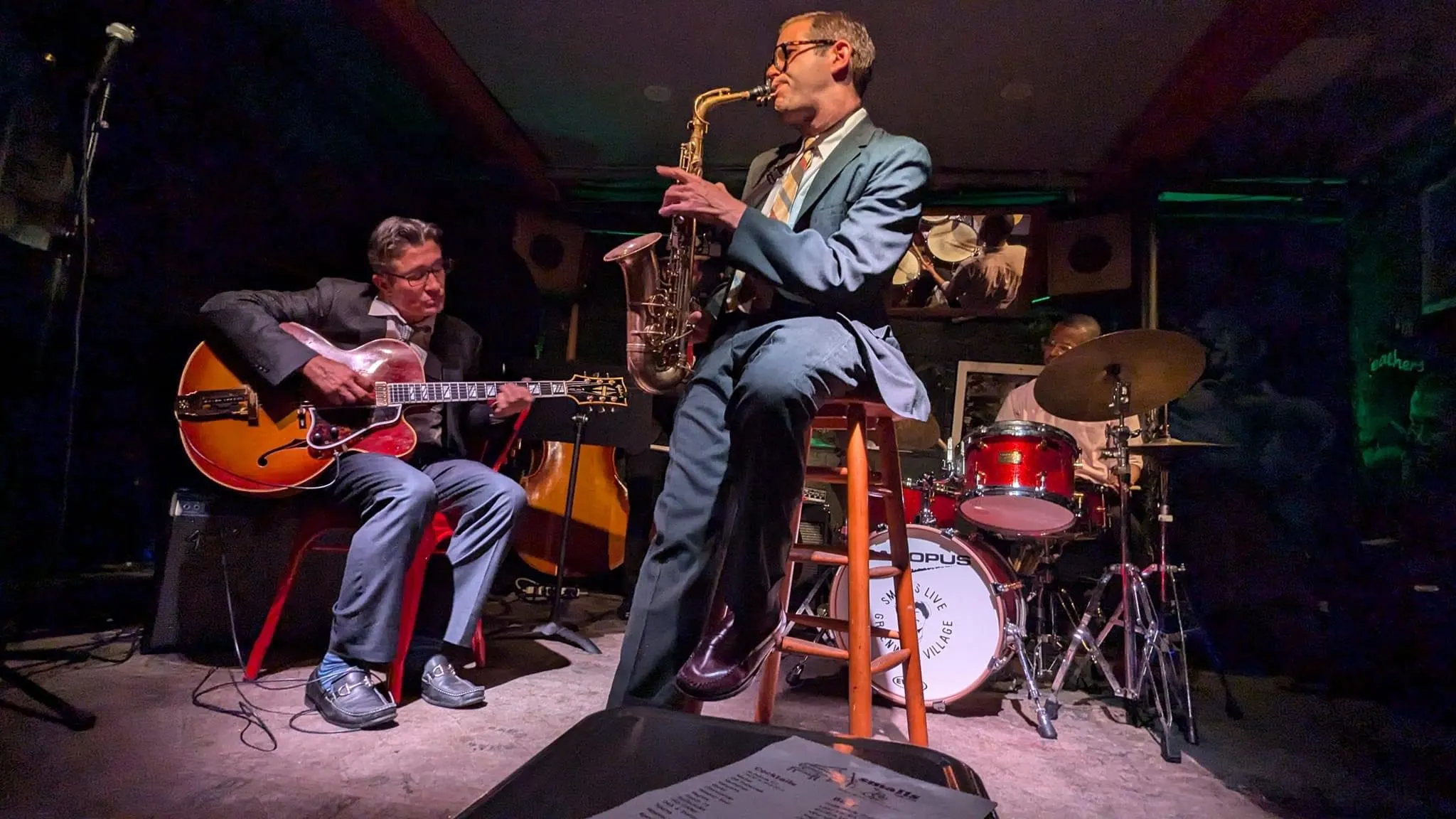 Aaron Johnson playing saxophone with a guitarist and rhythm section under stage lights.