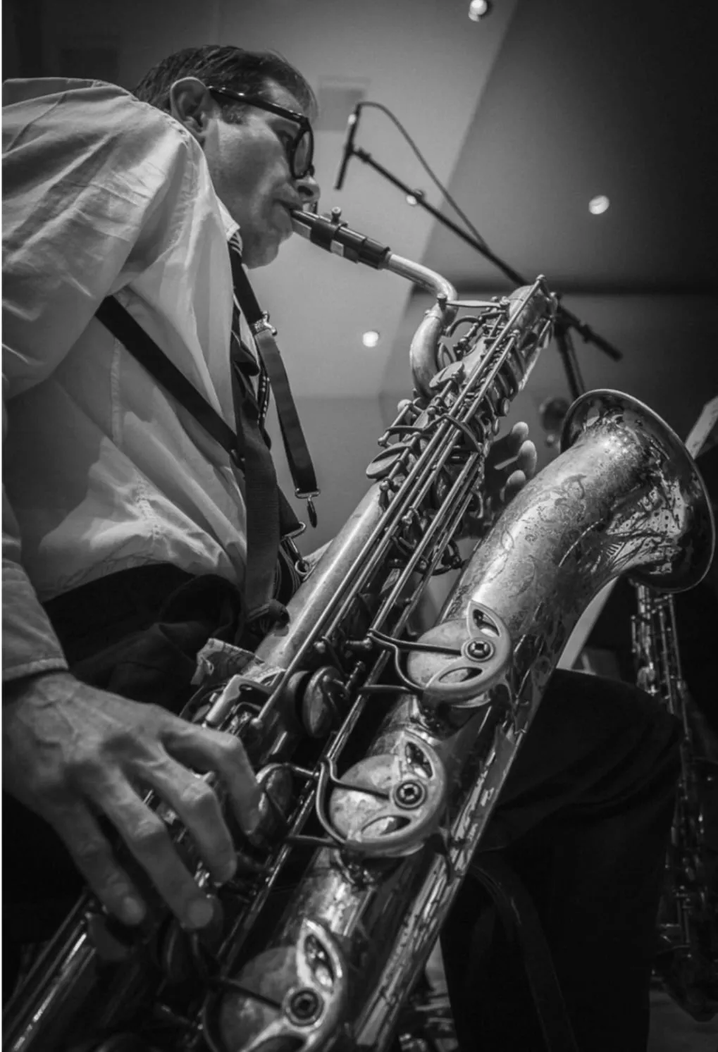 Close black and white photograph of Aaron Johnson playing baritone saxophone into a studio microphone.