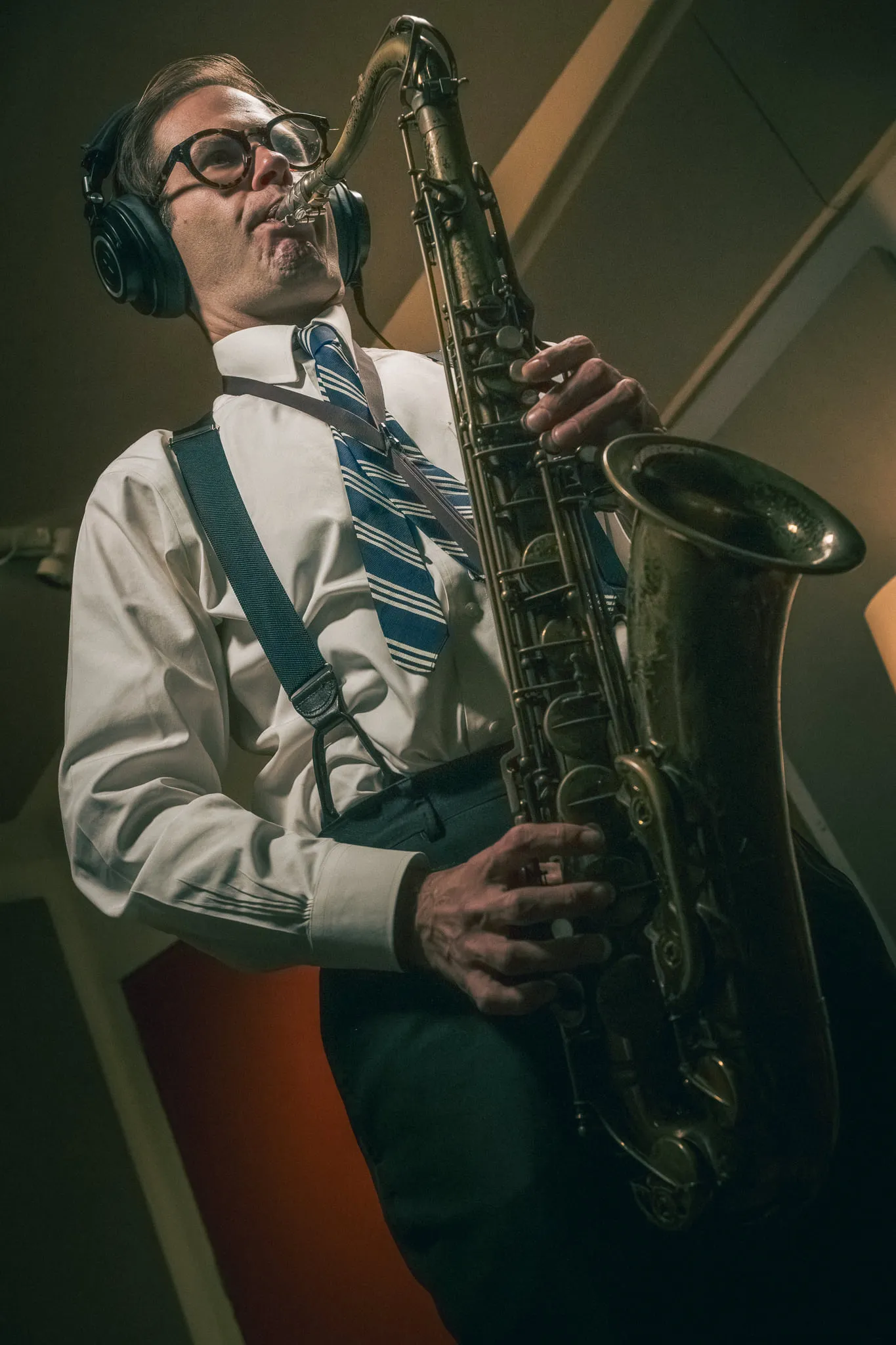 Aaron Johnson in headphones and braces playing baritone saxophone in a recording booth.