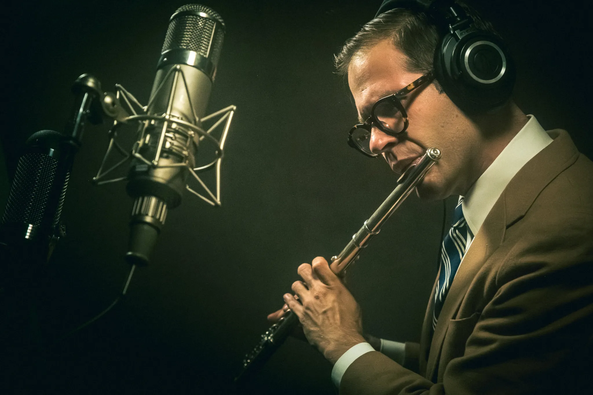 Aaron Johnson in headphones playing clarinet into a gold ribbon microphone.