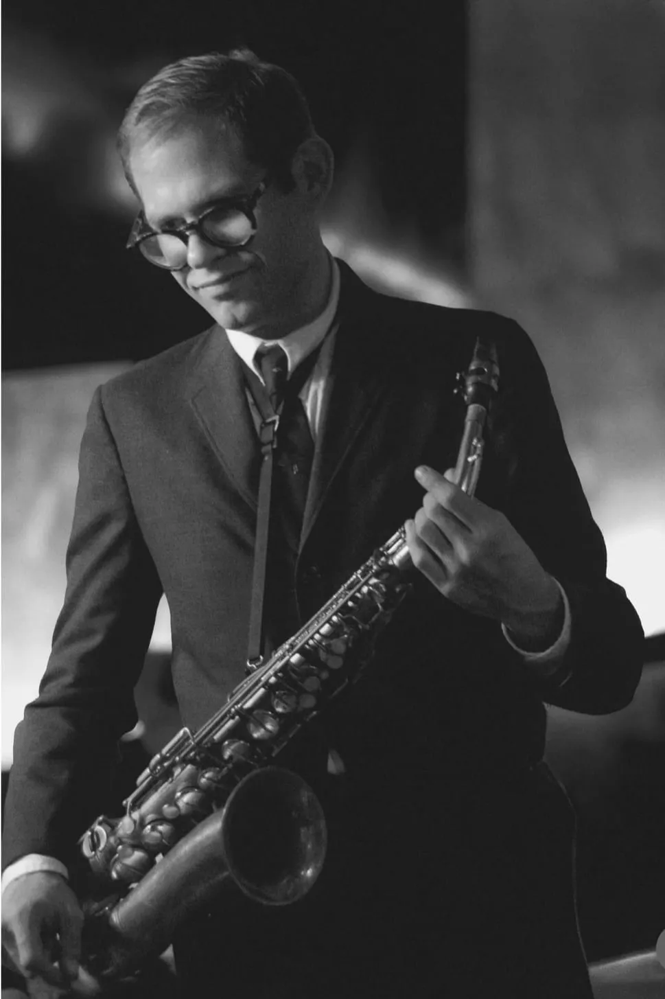 Aaron Johnson smiling with an alto saxophone against a dark background, in black and white.