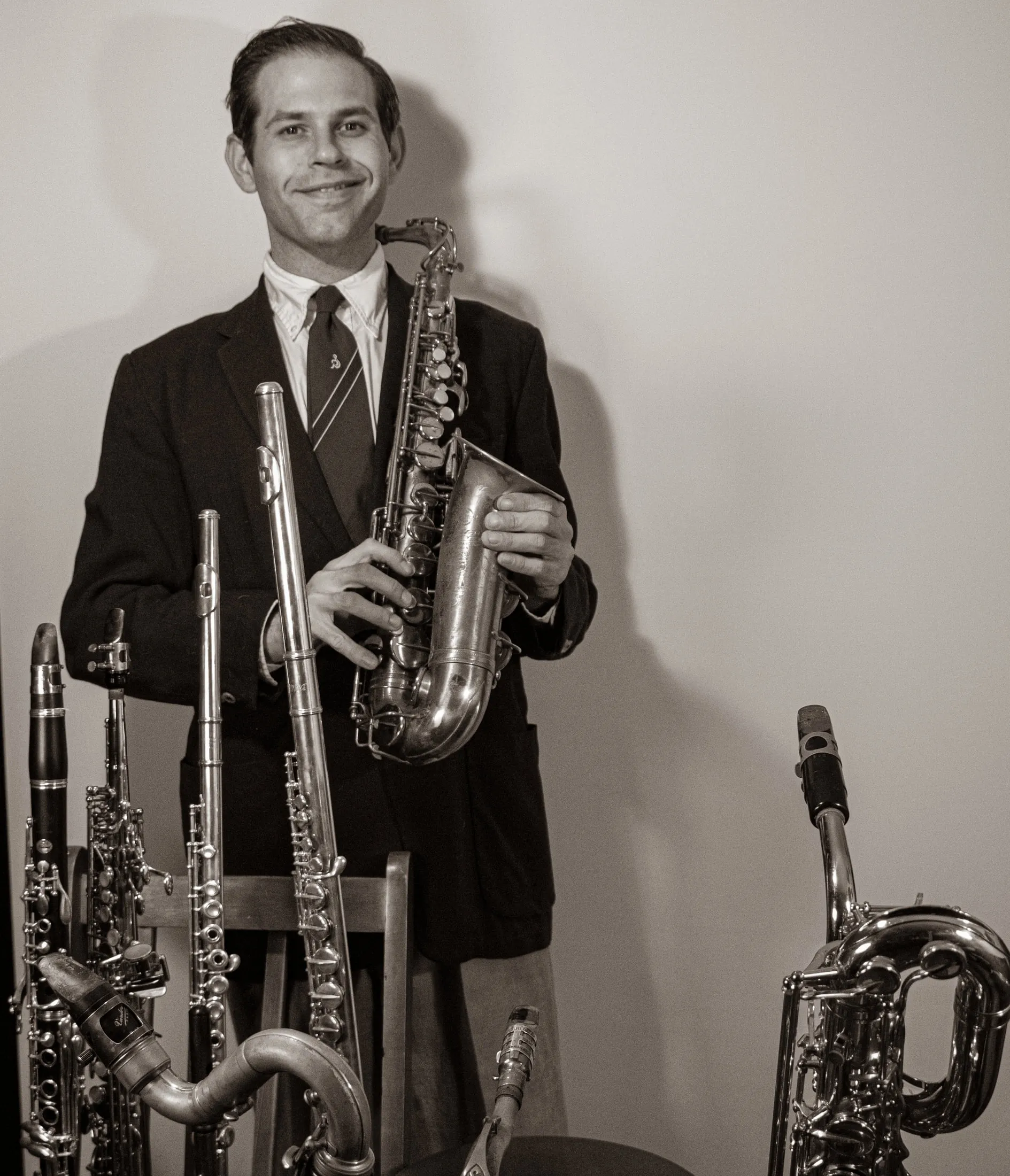 Aaron Johnson holding an alto saxophone among his rack of doubling instruments, looking to camera.