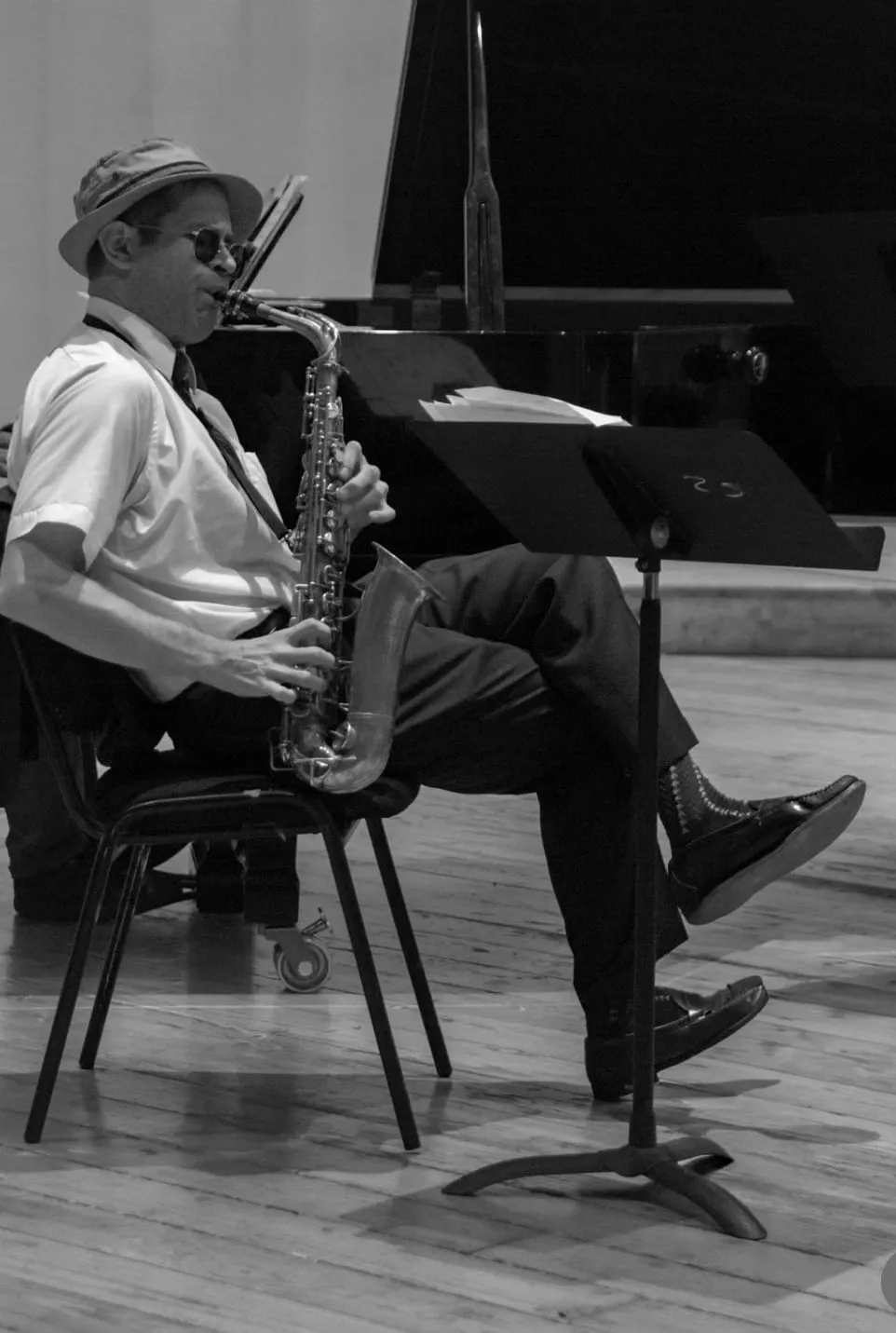 Aaron Johnson seated on stage playing alto saxophone from a music stand, in black and white.